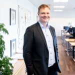 Smiling businessman standing confidently in a bright, modern office setting.