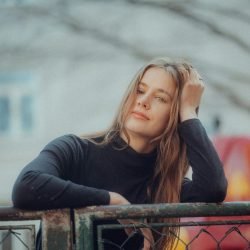 Stylish woman posing against a fence in an urban setting wearing a black sweater.