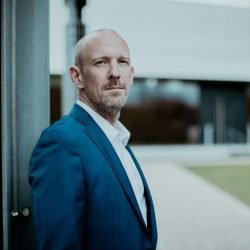 Middle-aged man in blue suit looking confident outside modern building.